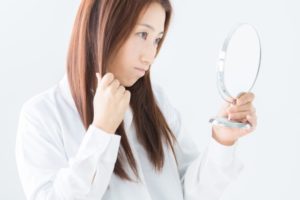 鏡で髪・頭皮をチェックする女性の写真画像